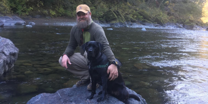 Justin and Hero Dogs Molly on a river rock